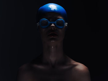 Close-up of shirtless man wearing sunglasses against black background