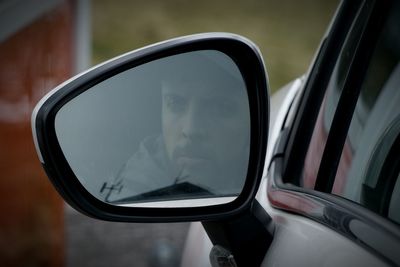 Man reflecting on side-view mirror of car