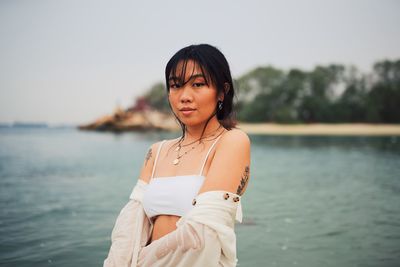 Portrait of young woman wearing bikini standing in sea against clear sky