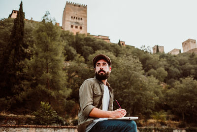 Man writing in book while sitting outdoors