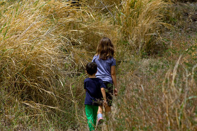 Rear view of children walking into tall grass