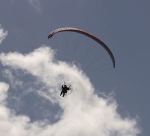 Low angle view of man paragliding in blue sky