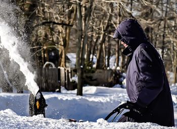Side view of man using snowblower in winter