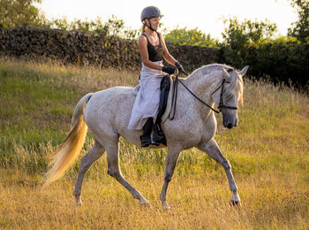 Dressage rider, female, on mare, trot on pasture outdoors.