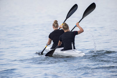 Rear view of female friends canoeing on sea