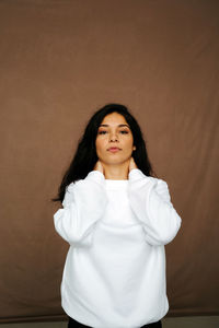 Calm ethnic female in trendy outfit standing on brown background and looking at camera in studio