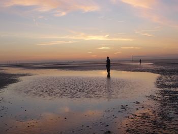 Silhouette man standing on beach against sky during sunset