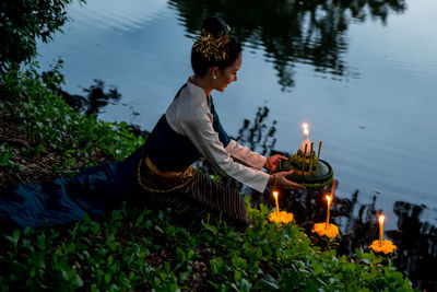 High angle view of woman sitting with candles by lake