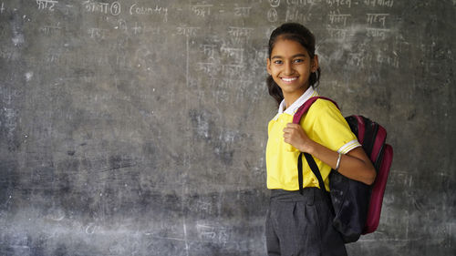 Smiling indian rural school girl with backpack looking at camera. 