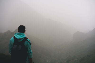 Rear view of mid adult man looking at mountains during foggy weather