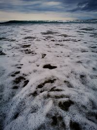 Footprints on sand at beach against sky