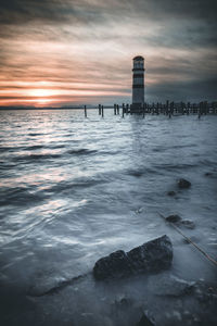 Lighthouse by sea against sky during sunset