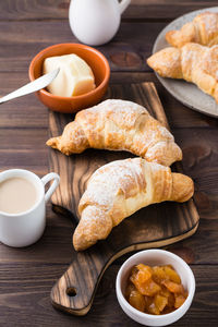 Fresh crispy croissants on a wooden board, a cup of coffee and jam in a bowl on the table