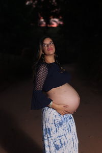 Pregnant young woman standing on field at night