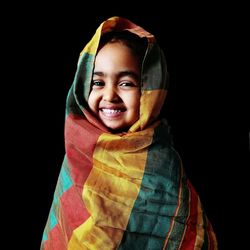 Portrait of cute smiling girl wrapped in scarf against black background