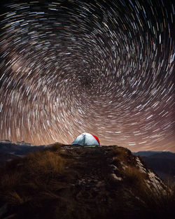 Star trails over landscape against sky at night