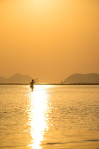 View of man standing in sea against sky during sunset