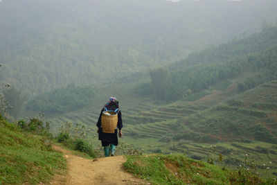 Rear view of woman carrying basket while walking on mountain