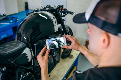 Side view of mature mechanic photographing motorcycle in garage