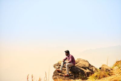 Man sitting on rock against mountains against clear sky