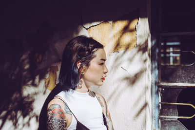 Thoughtful young woman with tattoos standing by old house