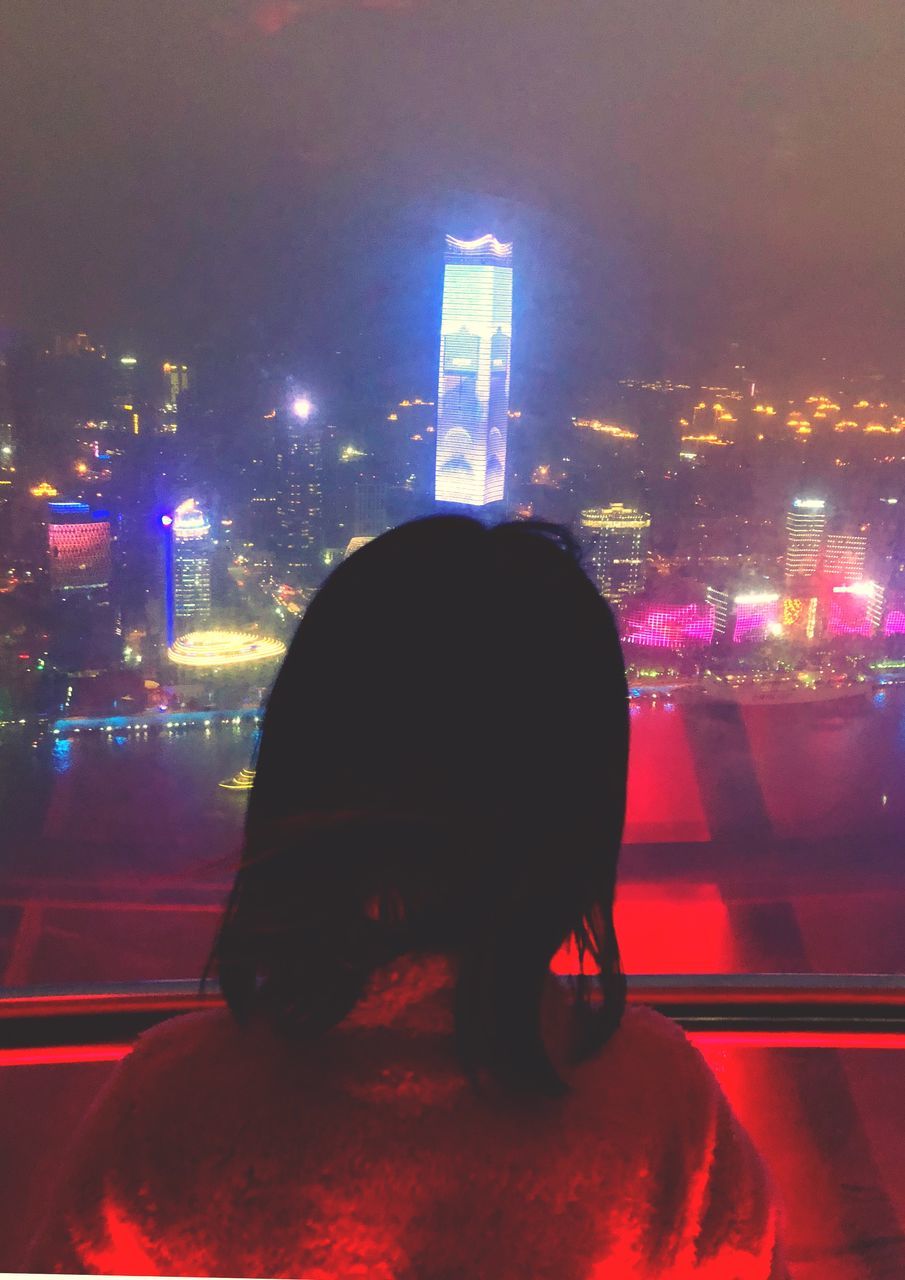 night, illuminated, city, architecture, built structure, building exterior, real people, one person, lifestyles, city life, adult, women, leisure activity, nightlife, street, rear view, window, sitting, hair, office building exterior, hairstyle, cityscape, skyscraper