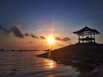 Silhouette built structure on beach against sky during sunset
