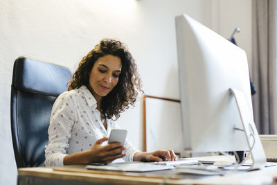 Successful businesswoman sitting in office, holding smart phone