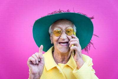 Portrait of smiling senior woman listening over phone against pink background