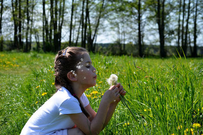 Side view of girl blowing dandelion while crouching on land