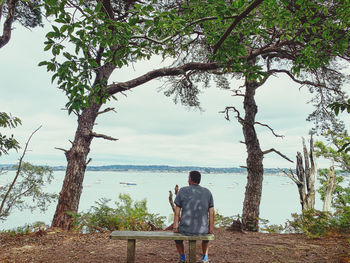 Rear view of man sitting on seat against sea