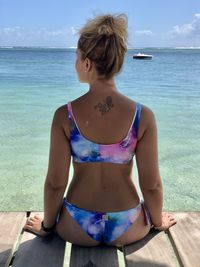 Rear view of woman sitting by sea against sky