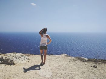 Rear view of woman standing on mountain by sea against sky during sunny day