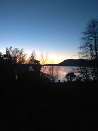 Silhouette trees by lake against sky during sunset