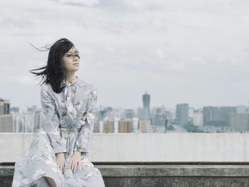 Young woman standing against sky in city