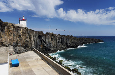 Scenic view of sea by rock formations seen from harbor against sky