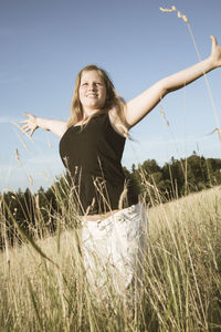 Smiling young woman standing on field against clear sky