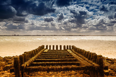 Pier on sea against cloudy sky