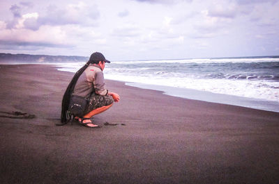 Man sitting at beach against sky