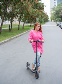 Portrait of smiling young woman riding push scooter on road