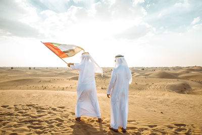 Man holding flag on sand dune against the sky