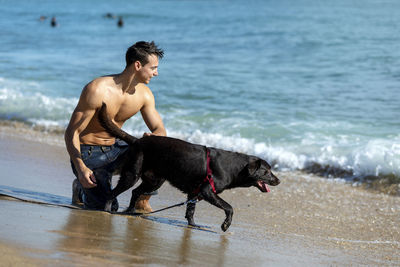 Shirtless man with dog at beach during vacation