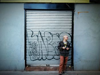 Smiling shaved head young man standing against graffiti on shutter