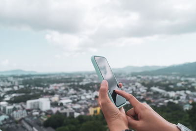 Midsection of man holding mobile phone against cityscape