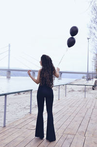 Full length of woman holding balloon while standing at beach against clear sky