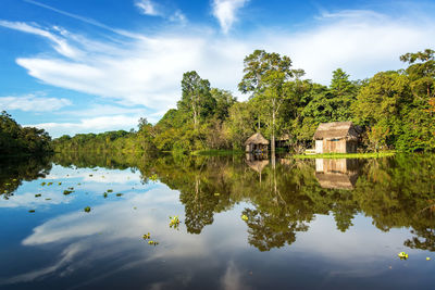 Yanayacu river by hut and trees with reflection against cloudy sky