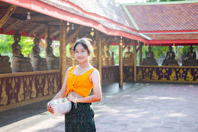 Portrait of young woman standing against building