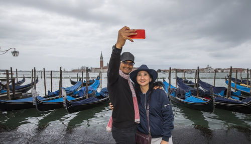 Thai couple taking selfie in front of parked gondola's in venice