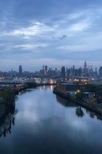 River by illuminated city against sky at dusk
