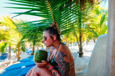 Close-up of woman drinking coconut water at beach during sunny day